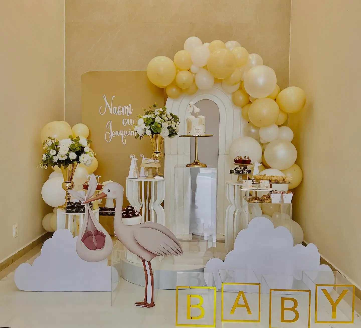 Mesa de chá de bebê com cegonhas, balões amarelos e brancos e letras BABY