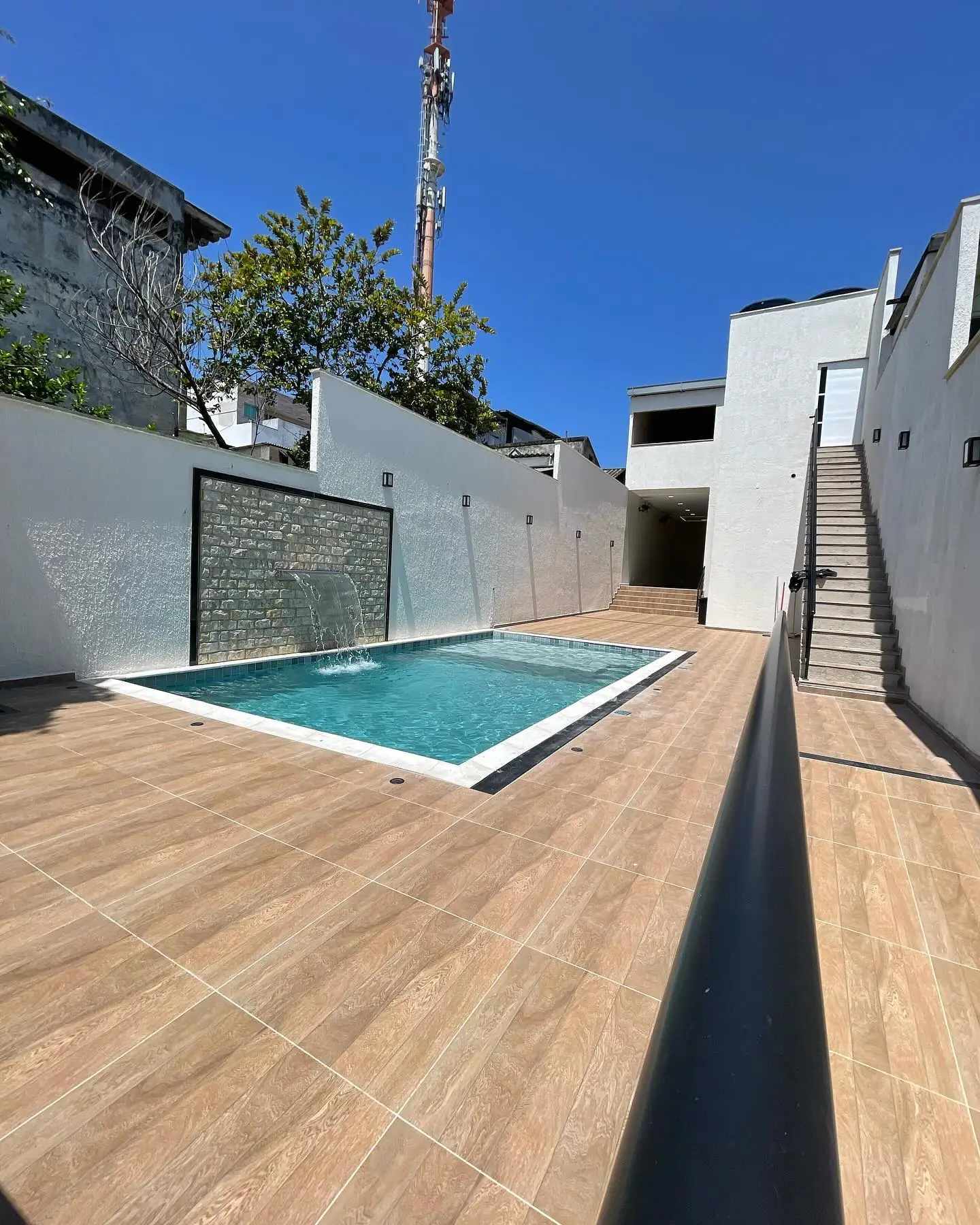 Piscina retangular com cascata e área externa revestida em piso de aspecto amadeirado