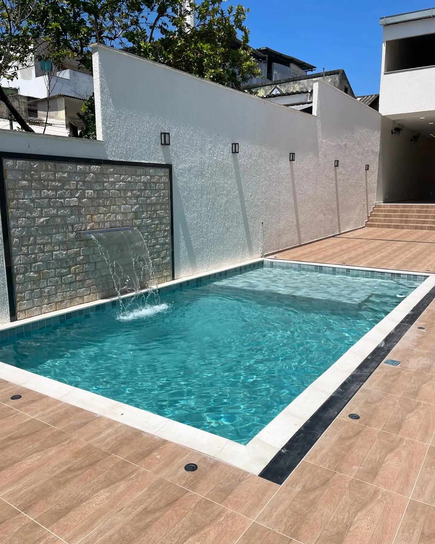 Vista lateral da piscina azul com cascata e revestimento de pedras